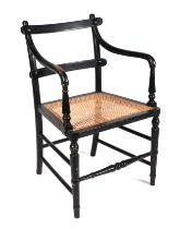 An Arts and Crafts Sussex style ebonised open arm chair, with cane seat, turned legs and front