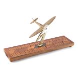 A trench art cast brass model of a Spitfire aircraft, mounted on a cribbage board, wingspan 13cm.
