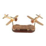 A pair of trench art cast brass models Wild Cat aircrafts, mounted on a cribbage board, 34cm wide.