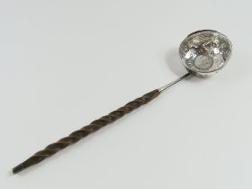 An angled silver ladle with coin in bowl’s centre,