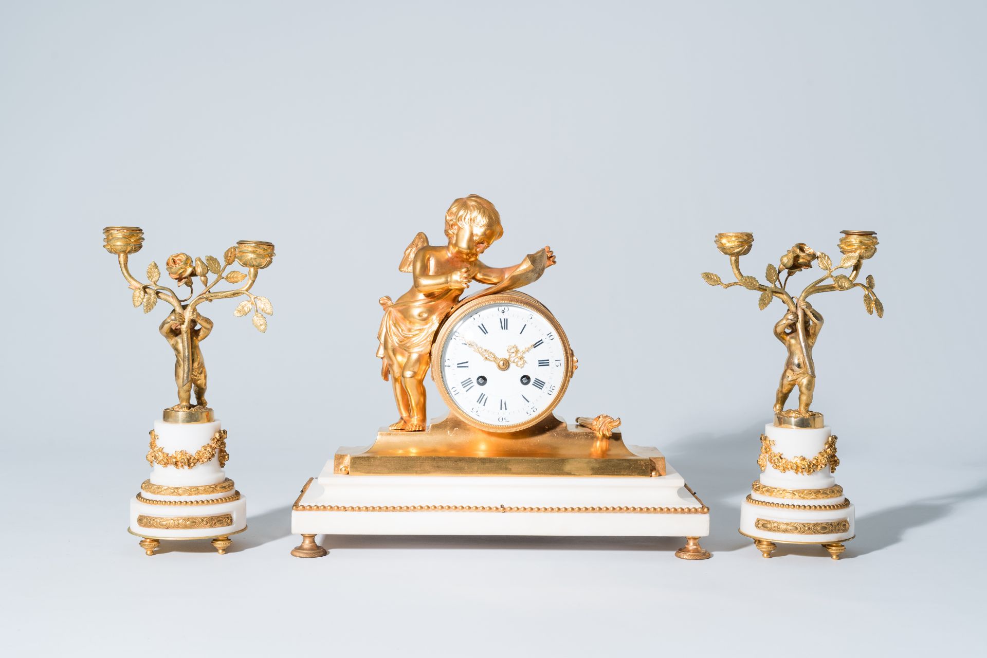 A French gilt bronze mounted white marble three-piece clock garniture with putti, 19th C.