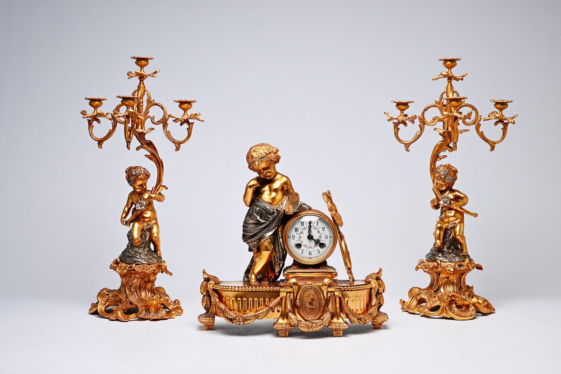 A French three-piece partly gilt metal clock garniture with putti, 20th C.