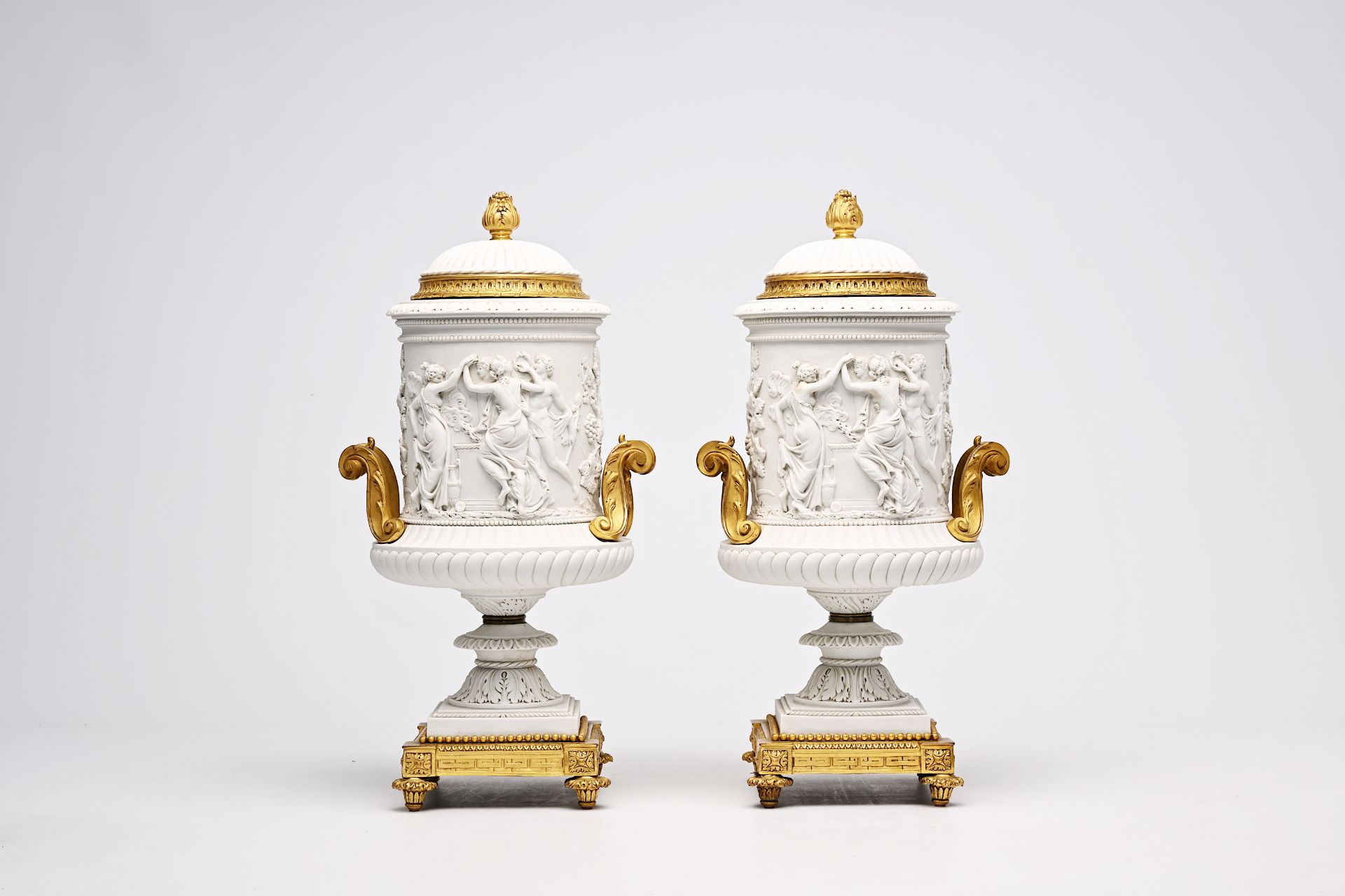 A pair of French biscuit gilt bronze mounted vases and covers with a frieze with bacchantes, Sevres