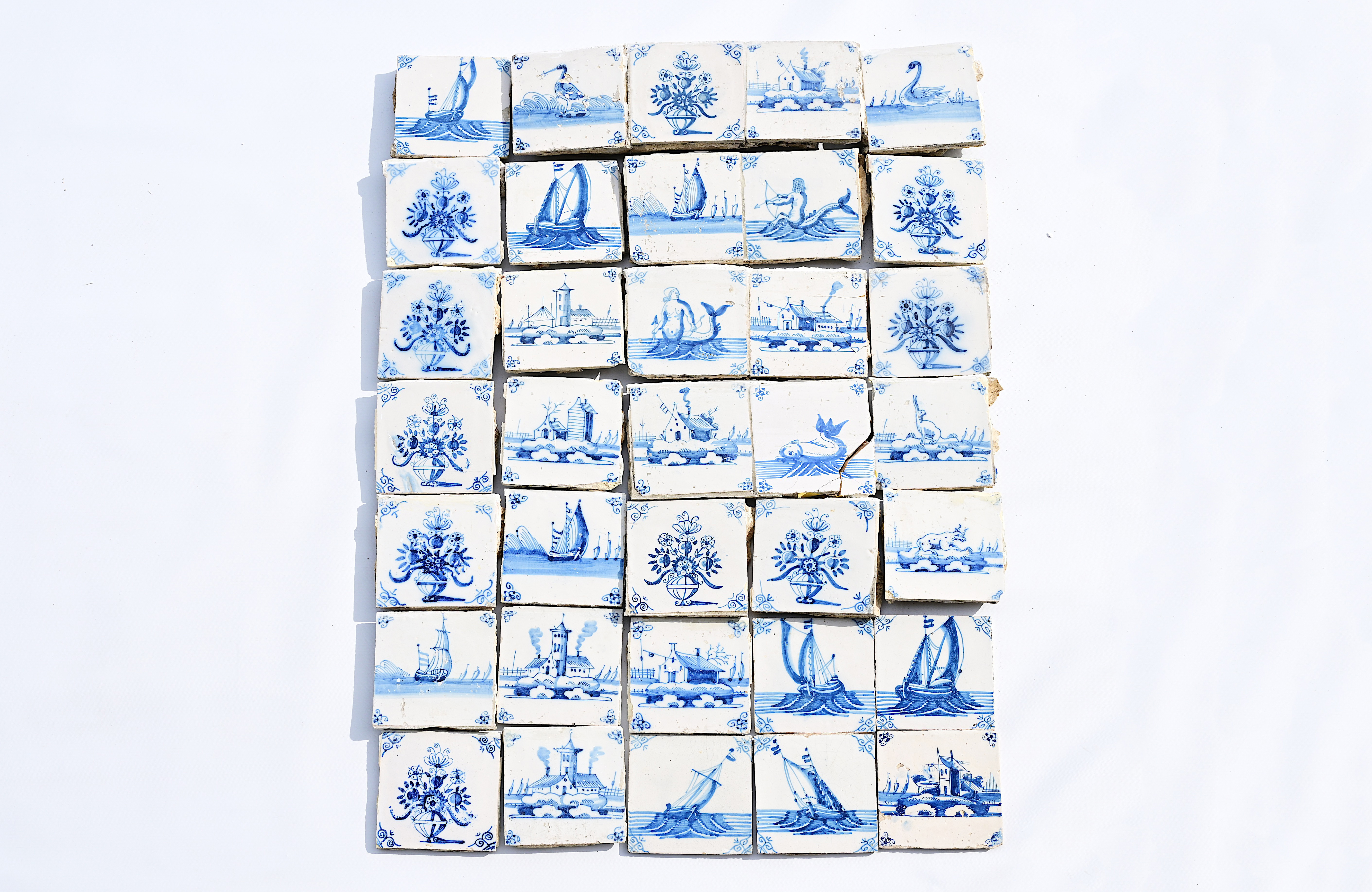 A varied collection of Dutch Delft blue and white tiles with flowers, boats, animals, sea monsters a