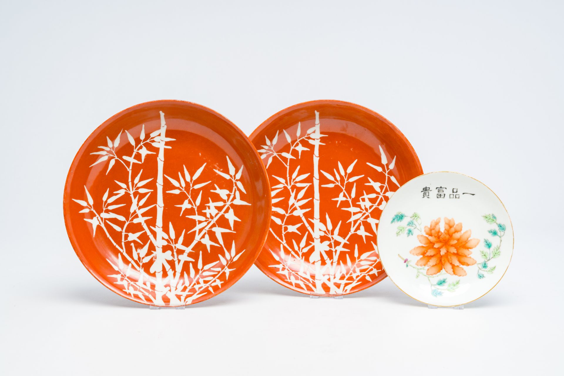 A pair of Chinese coral red ground 'bamboo' plates and a famille rose 'peony' saucer, 19th/20th C.