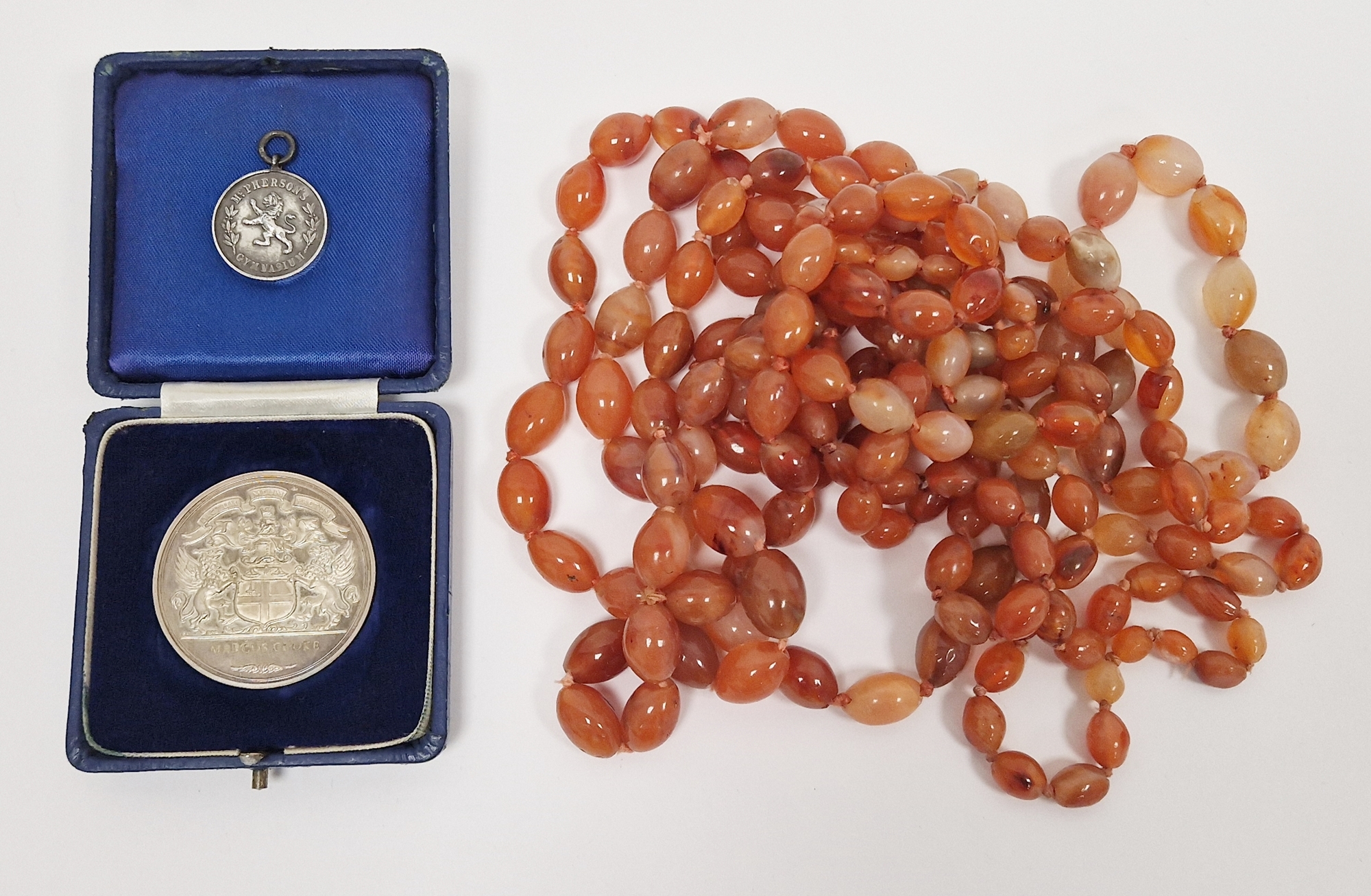 Three various long strings of cornelian beads, oval and strung, a silver commemorative medallion '