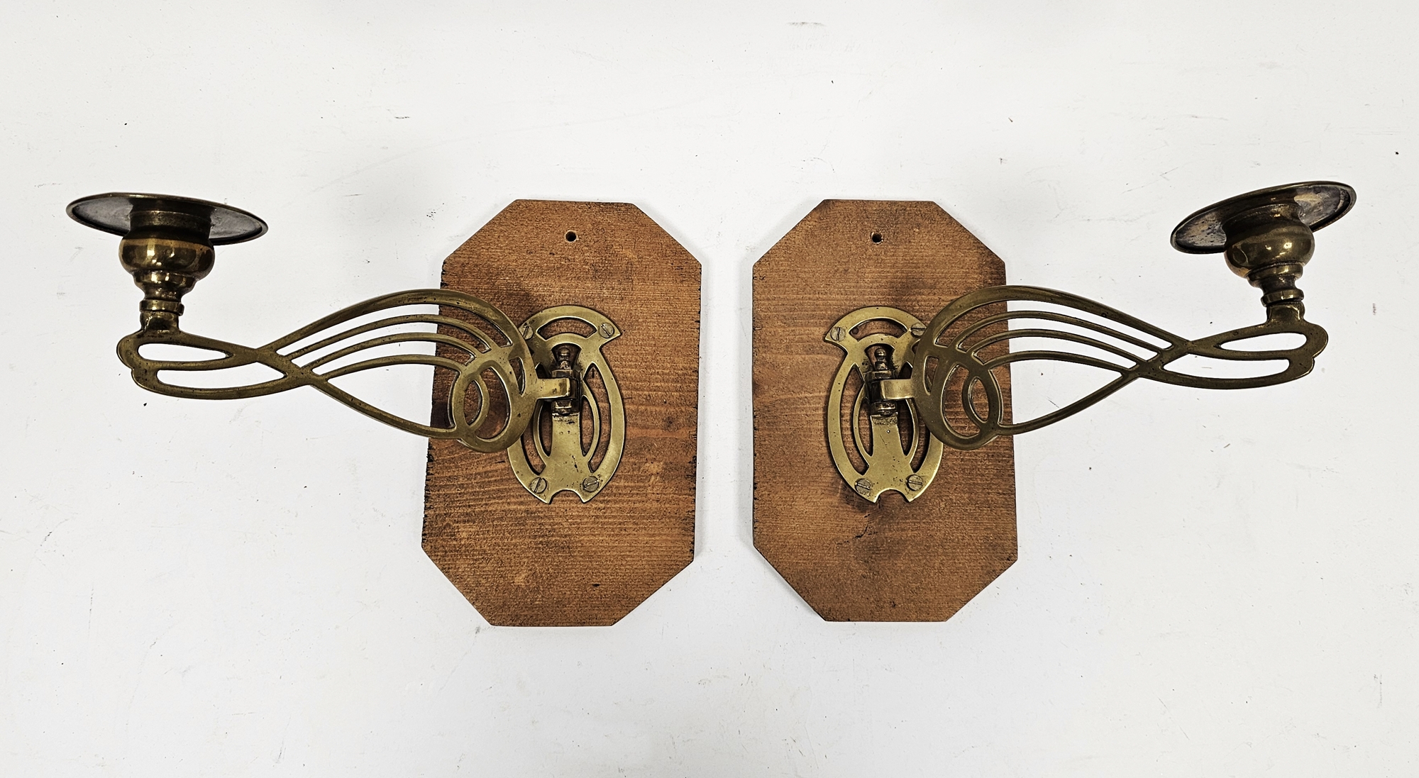 Pair of Art Nouveau brass wall lights each with pierced whiplash decoration, on later pine mounts,
