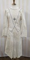 A 1920's cotton white dress piped with navy blue and a monogram in the centre, tie waist to the