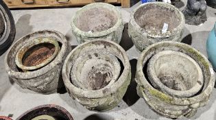 Five large weathered composite stone plant pots, one bearing swag decorations, the others bearing