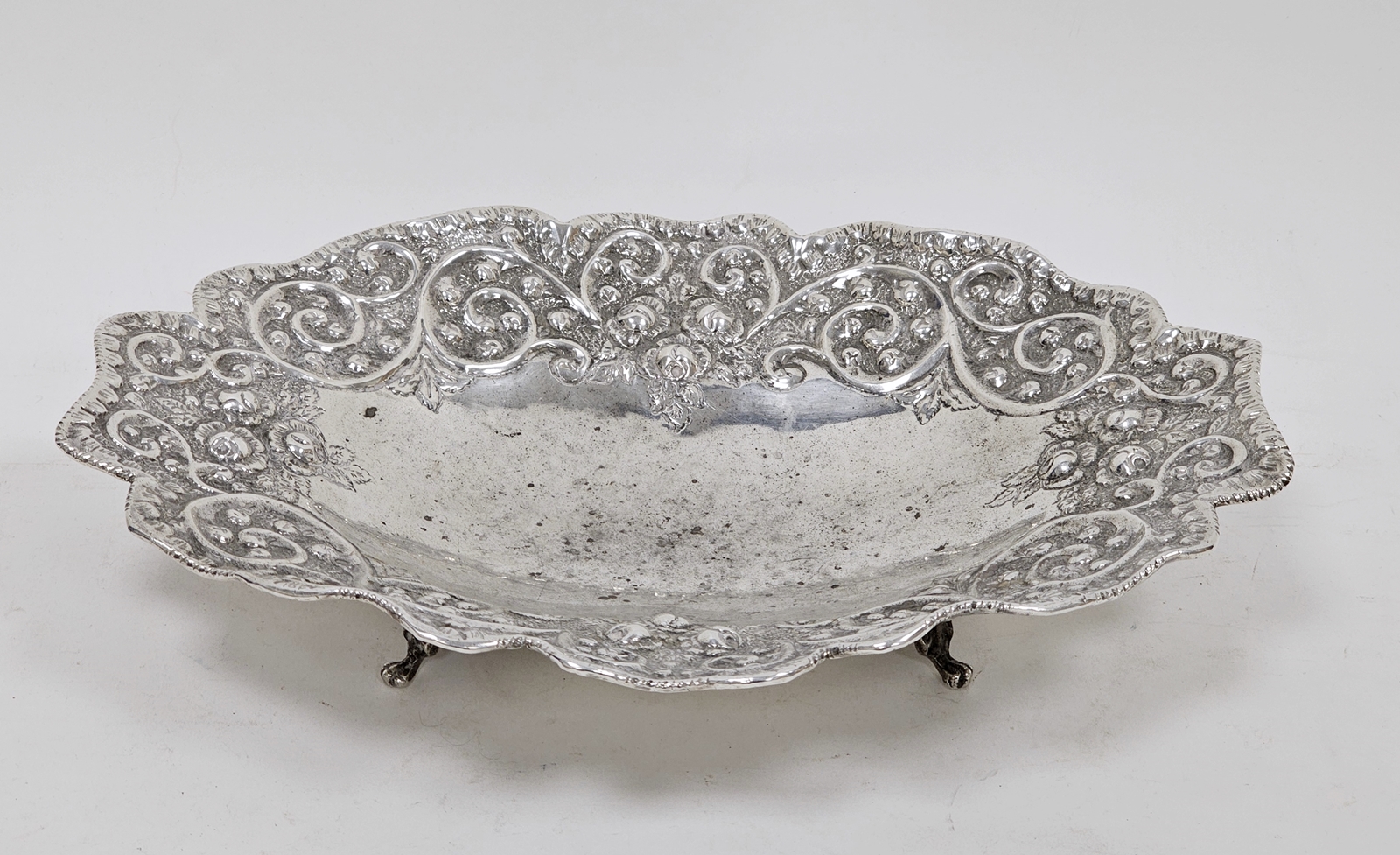 White metal shaped oval bowl with floral and scrolling decoration, on four bracket feet, marked 925,