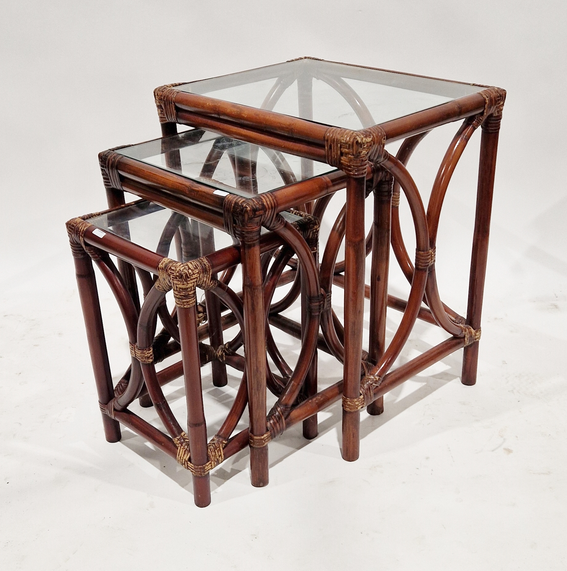Nest of three stained bamboo-effect occasional tables, each of rectangular form with glass tops,