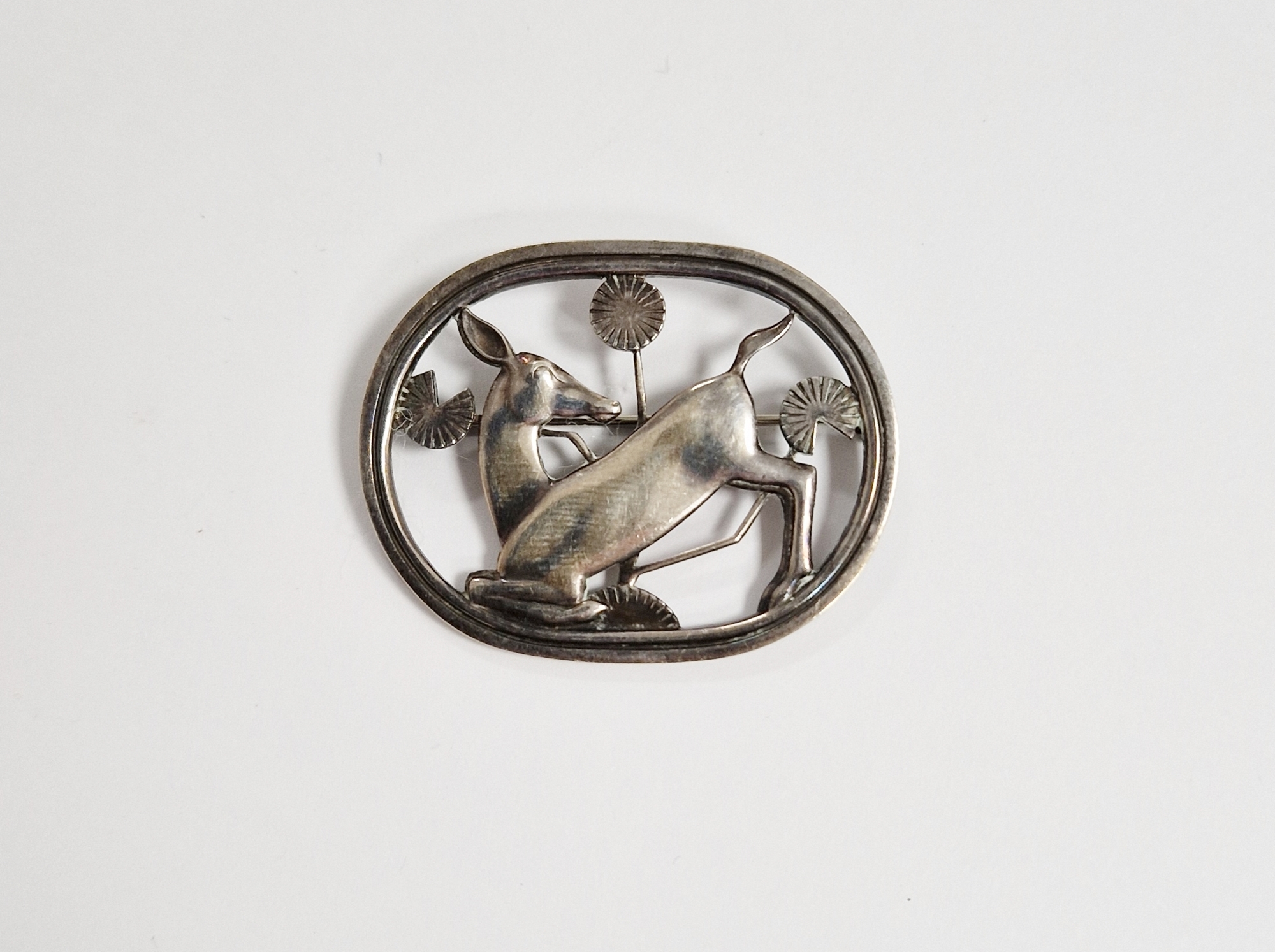 Georg Jensen silver brooch in the form of kneeling fawn within oval openwork surround, 4.5cm wide