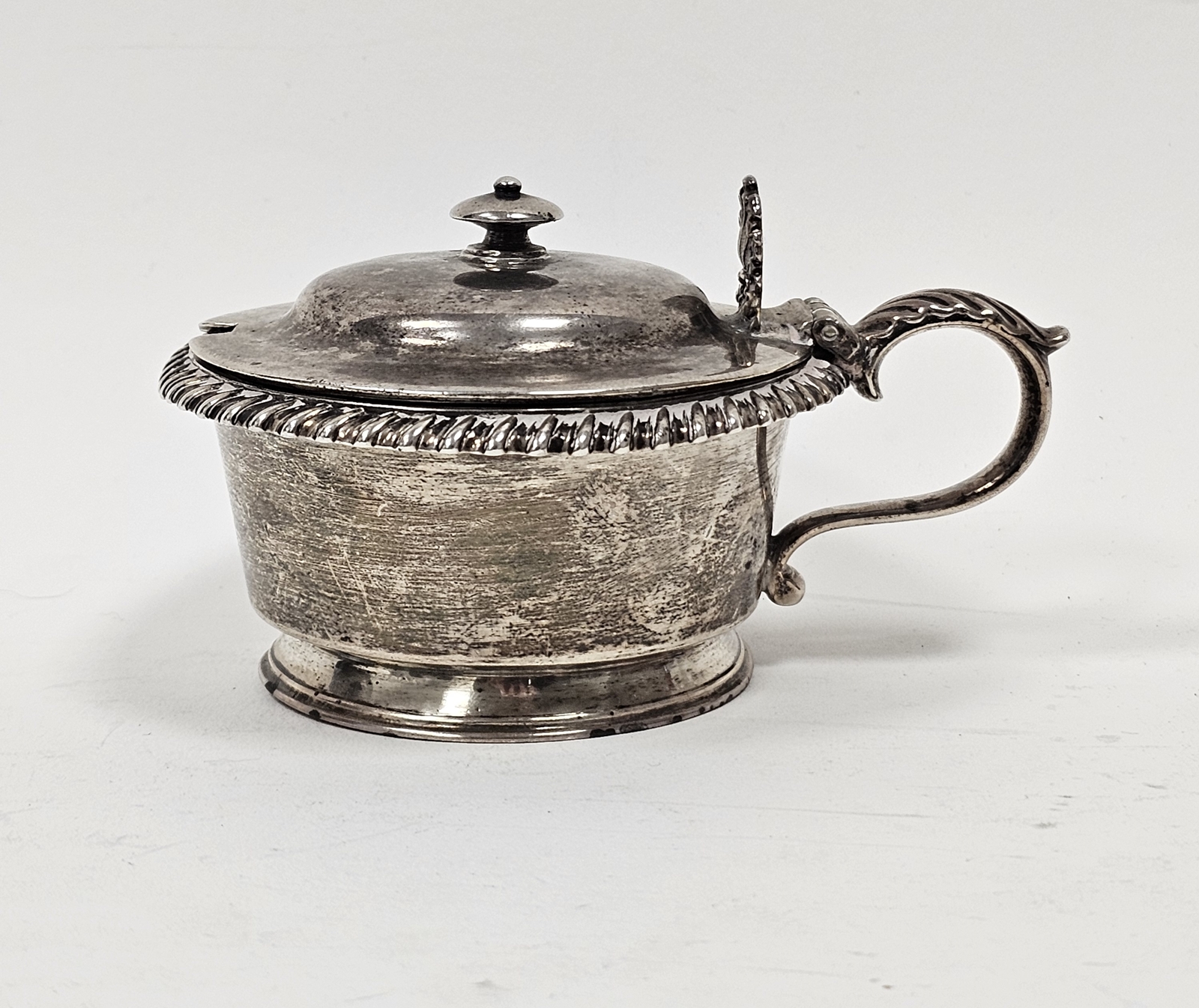 A William IV circular silver mustard and cover, the hinged cover with knop finial, shell and foliate