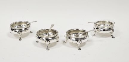 A set of four George V circular silver open salts, with clear glass liners and spoons, raised on