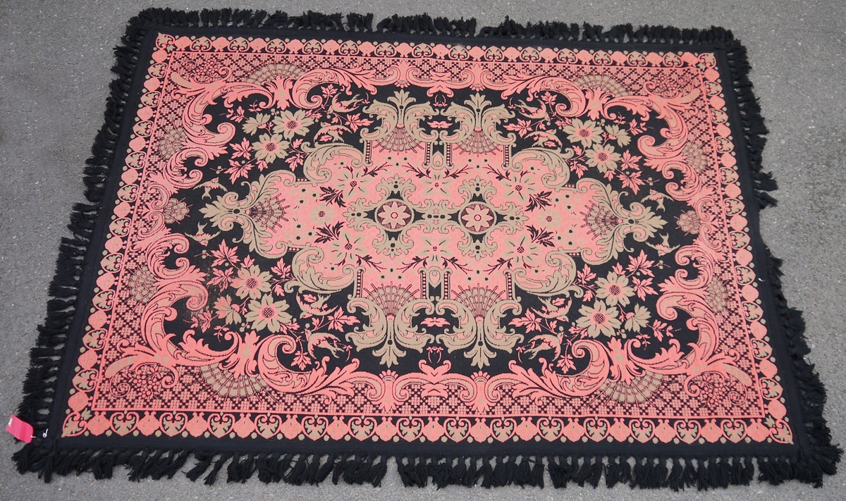 Woven wool rug in pink, black and green with large foliate scroll sided arabesque to the centre,