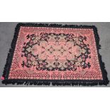 Woven wool rug in pink, black and green with large foliate scroll sided arabesque to the centre,