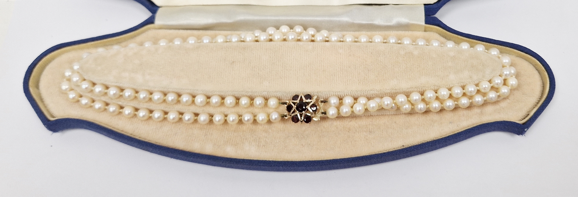 Double string of cultured pearls with 9ct gold and garnet set clasp, with star design, cased