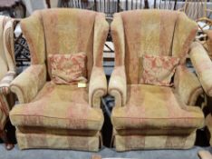 Modern pair of wing back armchairs, upholstered in a gold and red fabric both raised on castors,