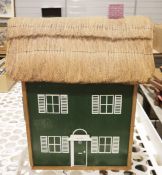 Wooden dolls house containing assorted furniture, green painted with thatched roof