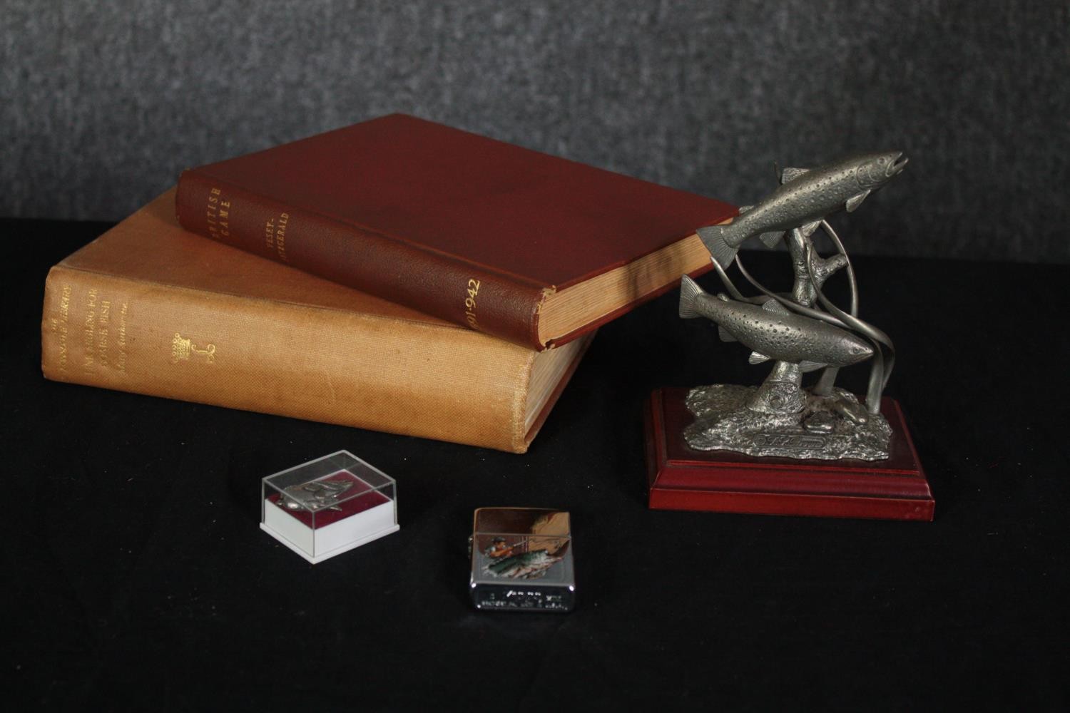 A miscellany. Two books on fishing and game hunting, a Zippo lighter and fish ornaments. H.22 W.
