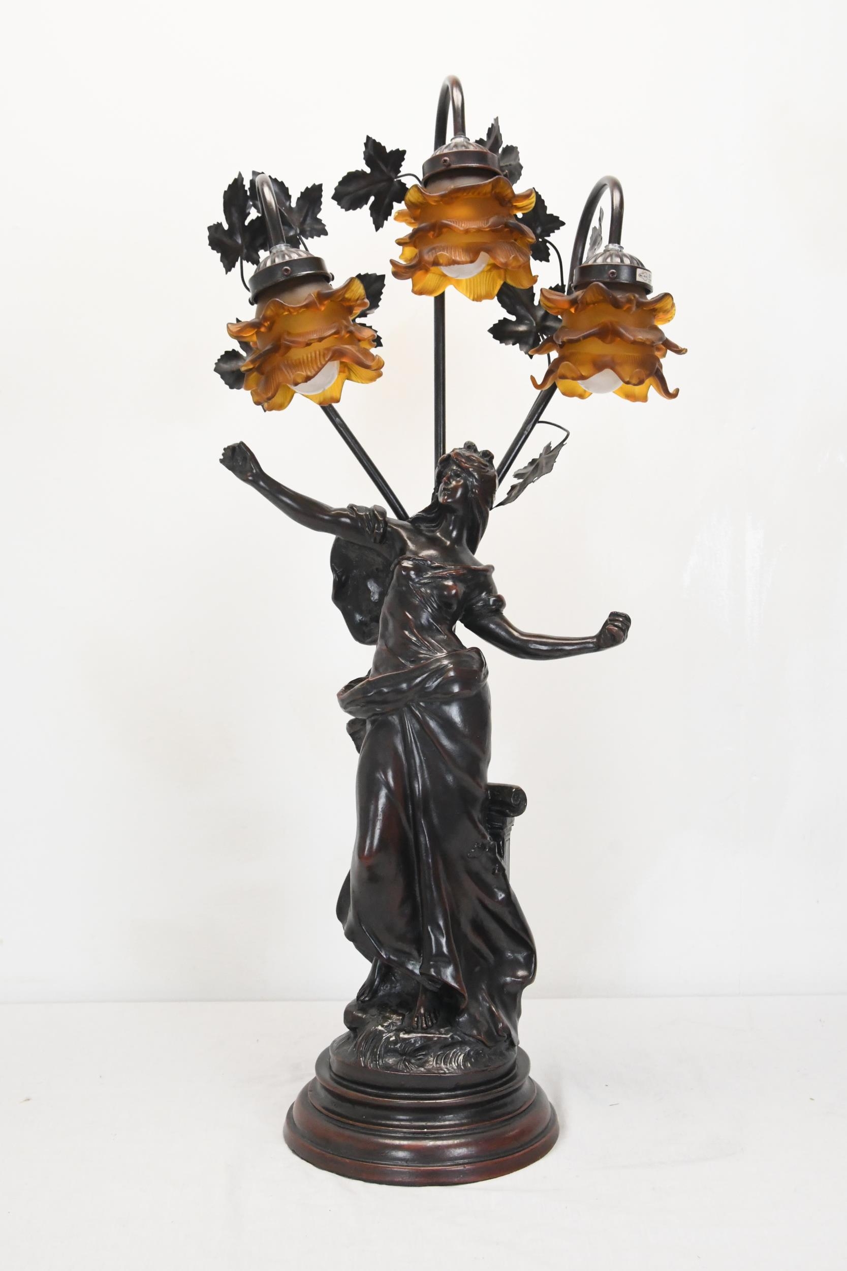 A 20th century spelter classical figural three branch table lamp, the floral shades of moulded amber