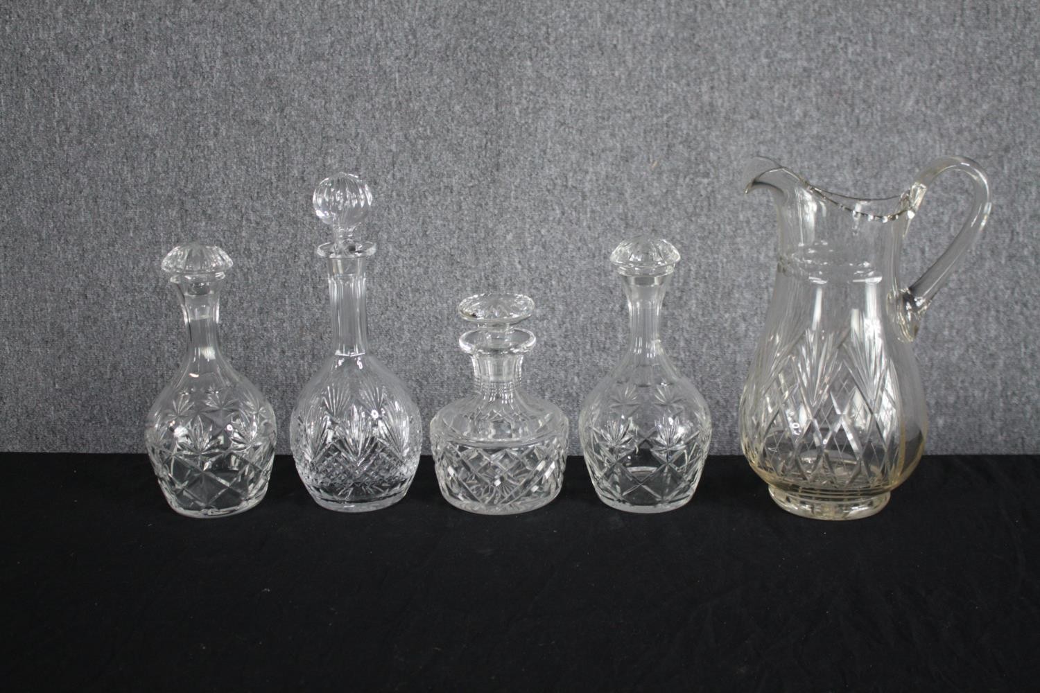 A mixed collection of four glass decanters and a jug. Cut glass and complete with their stoppers.