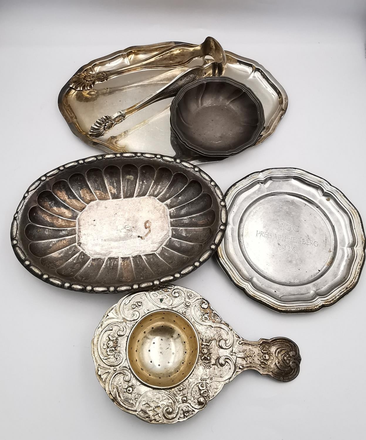 A collection of silver and white metal items, including a pair of sugar tongs with engraved