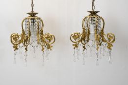 A pair of hanging ceiling lights with scrolling gilt metal frames and crystal drops. H.62 W.30cm.