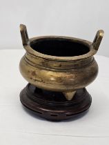 A Chinese twin handled bronze censer with tripod legs on a carved hardwood stand, Xuande marks to