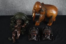 A cherub sconce lamp with A carved elephant and a pair of carved Chinese faces. H.39cm. (largest)