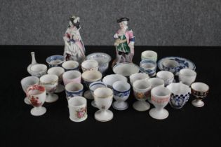 A collection of hand painted and printed egg cups, side plates and two figurines. H.16cm. (largest)