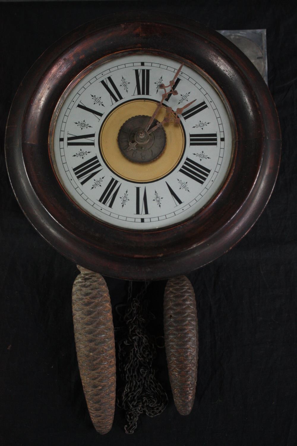 A 19th century Black Forest postman's alarm clock with black Roman numerals and fir cone weights.