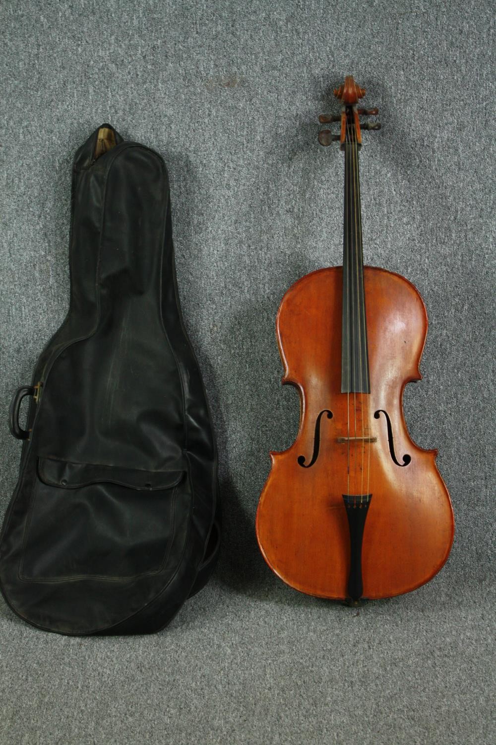 A cello in a soft case with no visible maker's mark. Road worn and with signs of being well