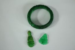 A small collection of jade consisting of a bangle and two seated Buddha figures. The bangle is