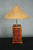 A table lamp fashioned from a four-part abacus with a woven rice picking hat type shade. The