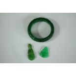 A small collection of jade consisting of a bangle and two seated Buddha figures. The bangle is