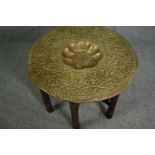 An Eastern brass embossed centre table on folding carved hardwood stand. H.57 Dia.80cm.