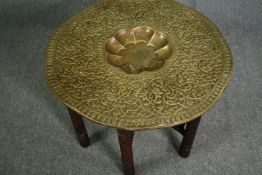 An Eastern brass embossed centre table on folding carved hardwood stand. H.57 Dia.80cm.