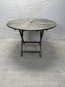 A vintage weathered teak folding garden table. H.75cm Dia.110cm.