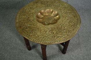 An Eastern brass embossed centre table on folding carved hardwood stand. H.57 Dia.80cm.