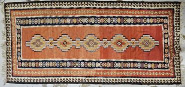 A flatweave Kelim carpet with repeating lozenge design on a terracotta ground. H.310 W.145cm.