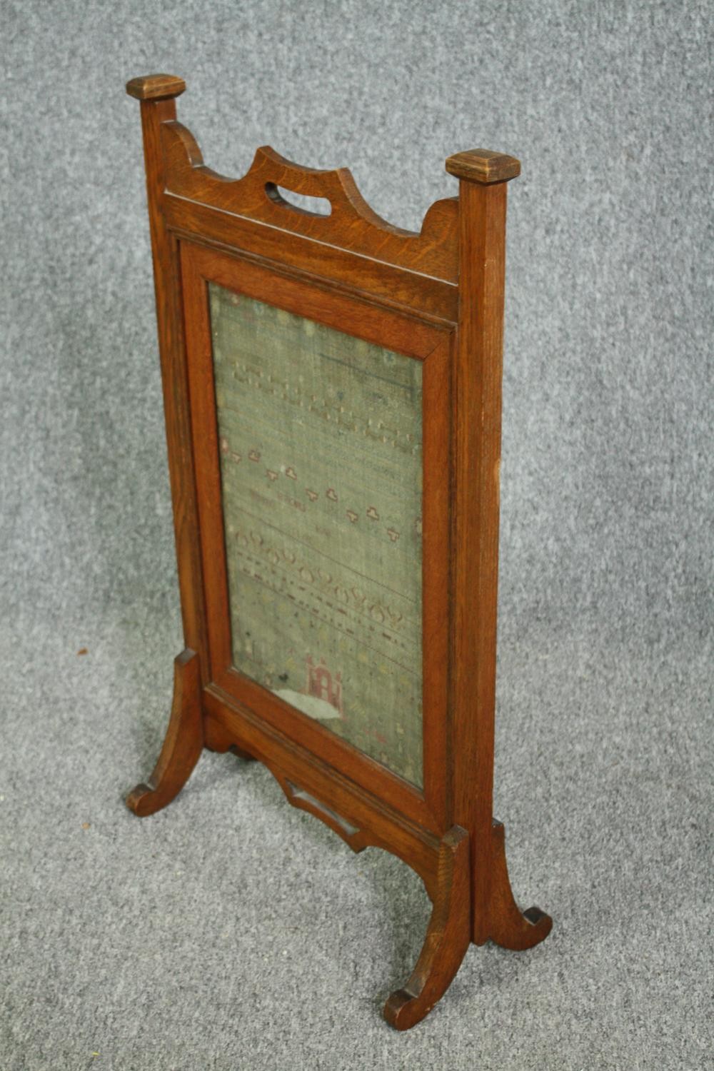 A late 19th century Arts and Crafts oak fire screen inset with a glazed needlework sampler. H.81 W. - Image 3 of 4