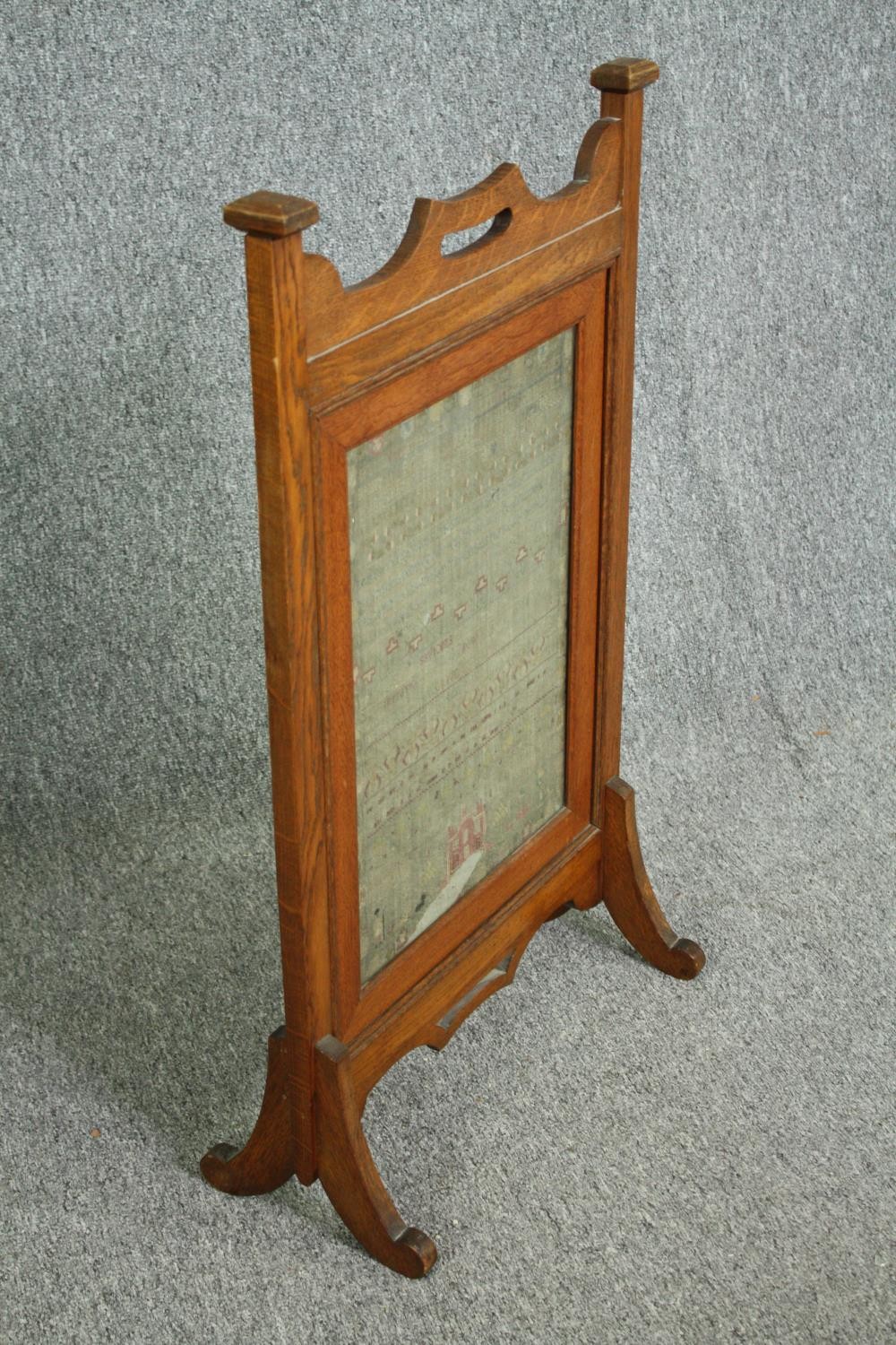 A late 19th century Arts and Crafts oak fire screen inset with a glazed needlework sampler. H.81 W. - Image 2 of 4