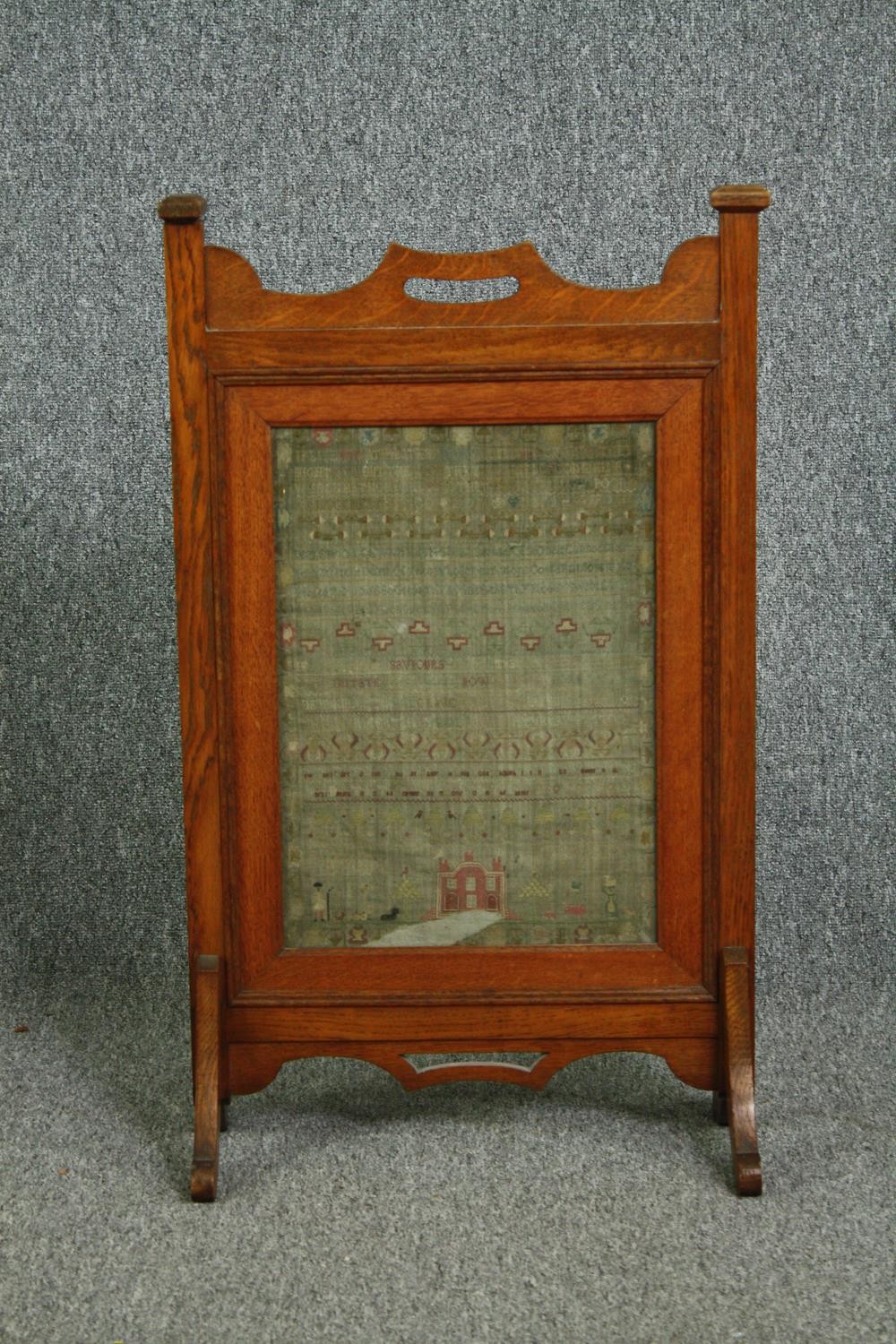 A late 19th century Arts and Crafts oak fire screen inset with a glazed needlework sampler. H.81 W.