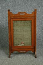 A late 19th century Arts and Crafts oak fire screen inset with a glazed needlework sampler. H.81 W.