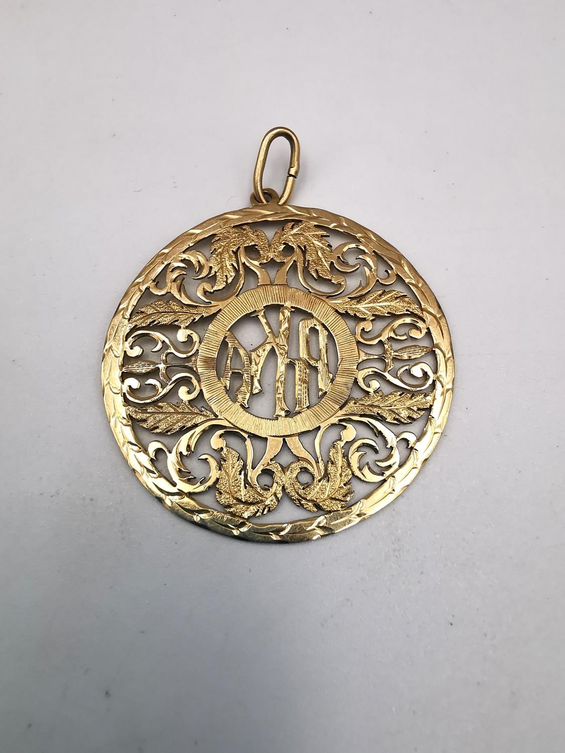 A gold plated pierced mongram pendant with acanthus leaf detailing. Diameter 4cm. Weight 5.06g