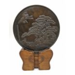 An early 20th century Japanese bronze Kagami mirror on wooden stand, decorated with a pine tree