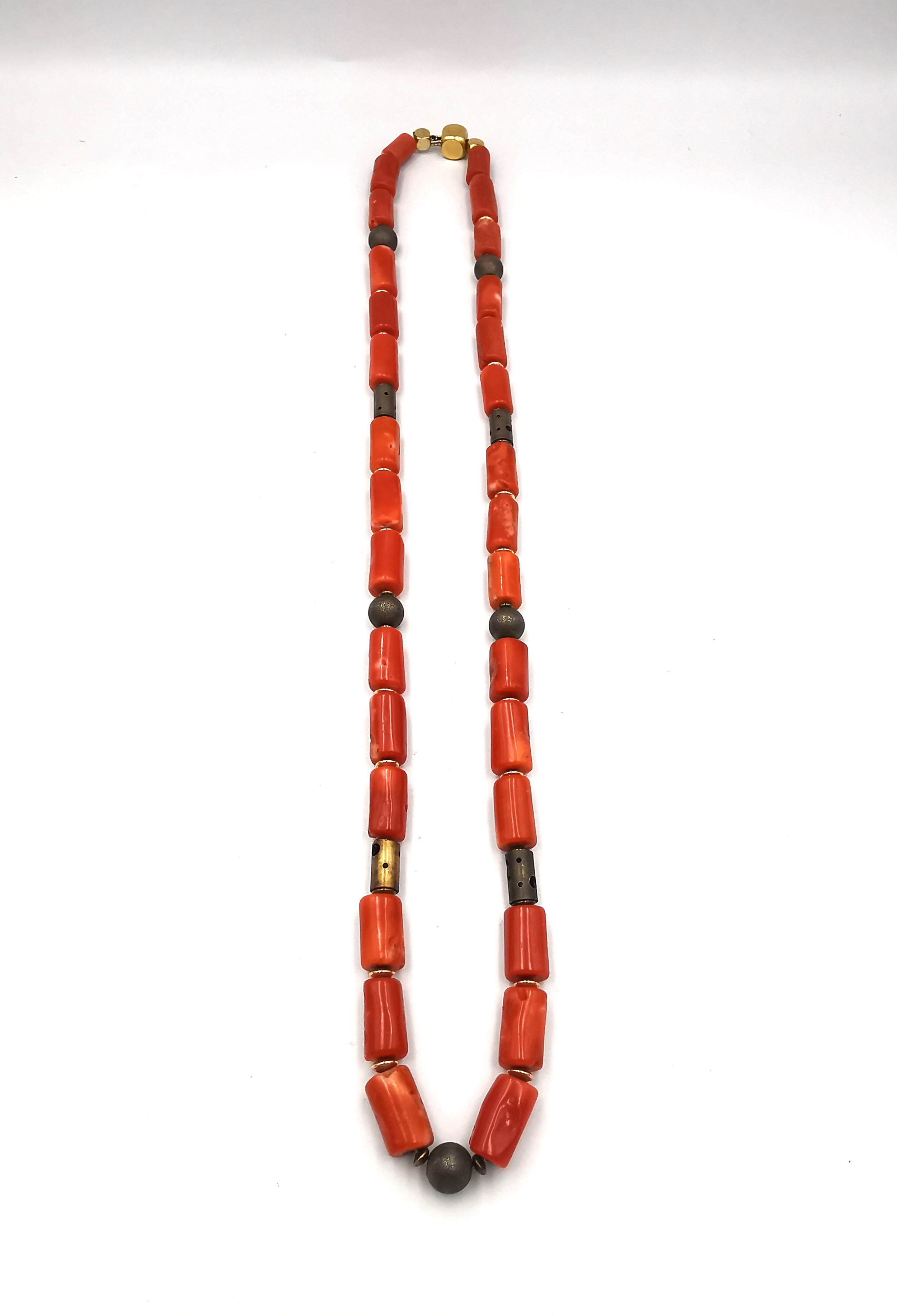 A vintage coral necklace with cylindrical metal pierced beads and gold plated spacers. Fastens