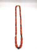 A vintage coral necklace with cylindrical metal pierced beads and gold plated spacers. Fastens