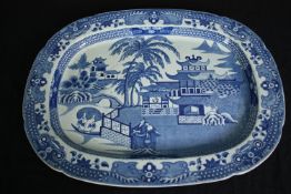 A large 19th century blue and white transfer printed serving platter with oriental figures in a
